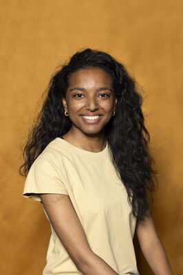 Portretfoto ensemblelid Alicia Boedhoe van Het Zuidelijk Toneel, die poseert tegen een okergele achtergrond.