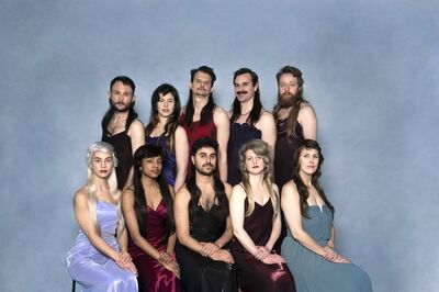 Groep van tien mensen in elegante jurken, poserende in een trendsetting stijl tegen een blauwe achtergrond.