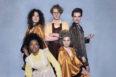 Vijf mensen in kleurige kleding poseren tegen een blauwe achtergrond. Hun stijlen zijn divers en expressief.