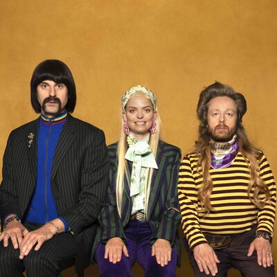 Acteurs Joep van der Geest, Keja Klaasje Kwestro en Louis van der Waal poseren tegen een okergele achtergrond.