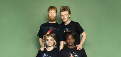 Vier performers staan in twee rijen voor een effen groene achtergrond. De twee personen achteraan rusten hun handen op de schouders van de twee personen vooraan. Ze dragen zwarte T-shirts met sciencefiction-achtige prints en kijken recht in de camera. Het beeld is onderdeel van de campagne voor de voorstelling Revenge of the Extras van Het Zuidelijk Toneel.