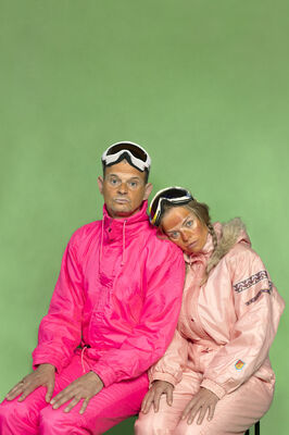 twee personen met fel roze ski pakken en ski brillen voor een groen doek