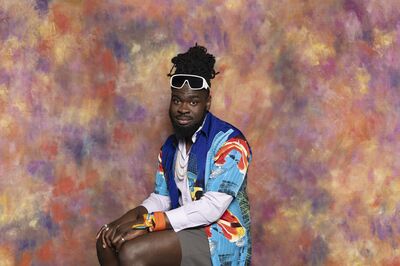 De performer Ousmane Bangura zit ontspannen voor een kleurrijke, schilderachtige achtergrond. Hij draagt een opvallend, blauw patroonhemd over een licht shirt, een korte broek, witte zonnebril en kleurrijk sjaaltje om zijn pols. Dit is het campagnebeeld van de educatievoorstelling Zo Dus van Het Zuidelijk Toneel.