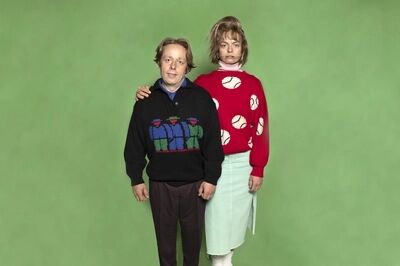 Twee mensen staan naast elkaar voor een groene achtergrond, één in een zwart vest en de ander in een rode trui met stippen.