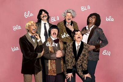 Zes performers in kleurrijke outfits, lachen en poseren voor een roze achtergrond met tekstballonnen met het woord "bla".