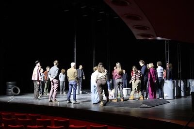 Groep acteurs in een theaterzaal tijdens een repetitie, omringd door scènes en decorstukken.