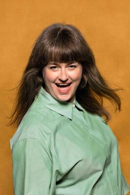 Portretfoto artistiek leider en directeur van Het Zuidelijk Toneel Sarah Moeremans, , poserend tegen een okergele achtergrond.