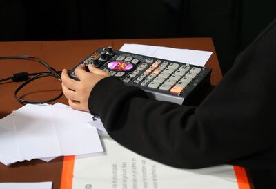 Een hand bedient een muzikale controller op een tafel, omringd door papier.