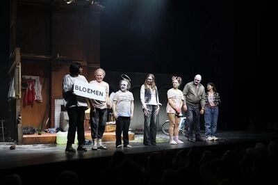 Performers staan op het podium met een bord met daarop 'Bloemen' bij het eindapplaus.