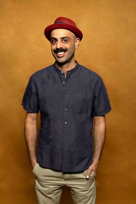 Portretfoto maker Enkidu Khaled van Het Zuidelijk Toneel, poserend met handen in zakken tegen een okergele achtergrond.