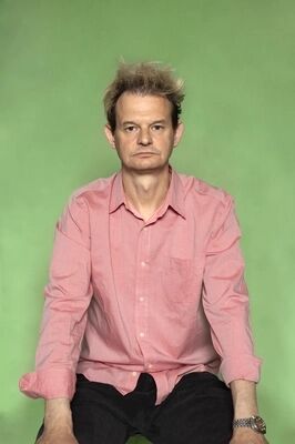 Portretfoto ensemblelid Gillis Biesheuvel van Het Zuidelijk Toneel, die een gekke bek trekt en poseert tegen een groene achtergrond.
