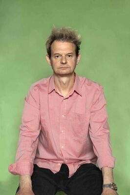 Portretfoto ensemblelid Gillis Biesheuvel van Het Zuidelijk Toneel, die een gekke bek trekt en poseert tegen een groene achtergrond.