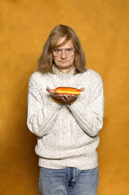 Portretfoto ensemblelid Gillis Biesheuvel van Het Zuidelijk Toneel, die poseert met een worstenbroodje tegen een okergele achtergrond.