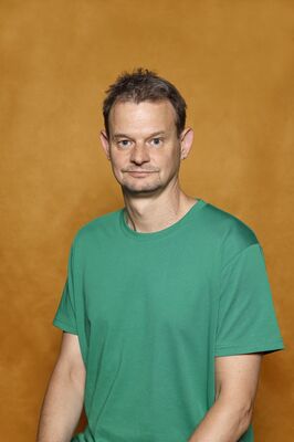 Portretfoto ensemblelid Gillis Biesheuvel van Het Zuidelijk Toneel, die poseert tegen een okergele achtergrond.