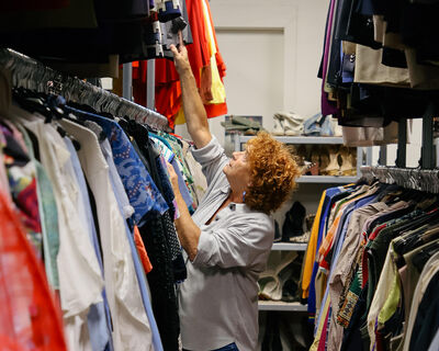 Een medewerker van de kostuumverhuur van Het Zuidelijk Toneel die tussen rekken vol theaterkostuums staat en kledingstukken selecteert of toont.