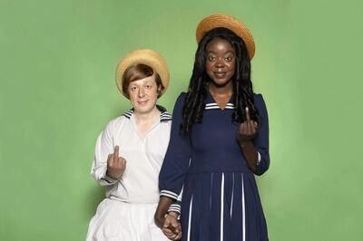Een man en vrouw zijn gekleed als jonge sailor kids, lachen lief naar de camera, houden elkaars hand vast en steken met hun andere hand de middelvinger op.