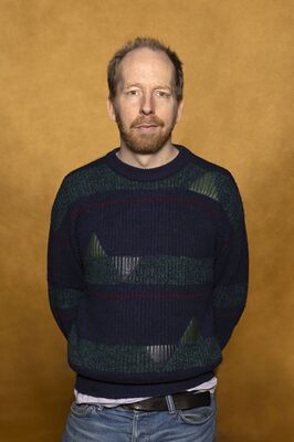 Portretfoto maker Jetse Batelaan van Het Zuidelijk Toneel, poserend tegen een okergele achtergrond.