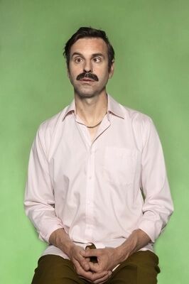 Portretfoto ensemblelid Joep van der Geest van Het Zuidelijk Toneel, die een gekke bek trekt en poseert tegen een groene achtergrond.