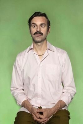 Portretfoto ensemblelid Joep van der Geest van Het Zuidelijk Toneel, die een gekke bek trekt en poseert tegen een groene achtergrond.