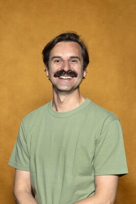 Portretfoto ensemblelid Joep van der Geest van Het Zuidelijk Toneel, die poseert tegen een okergele achtergrond.