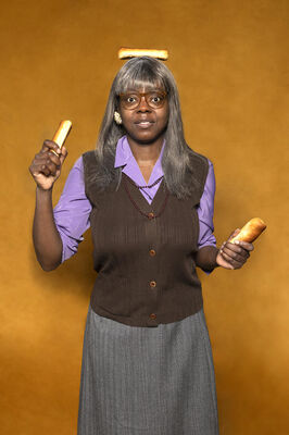 Portretfoto ensemblelid Julia Ghysels van Het Zuidelijk Toneel, die poseert met worstenbroodjes tegen een okergele achtergrond.