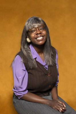 Portretfoto ensemblelid Julia Ghysels van Het Zuidelijk Toneel, die poseert tegen een okergele achtergrond.