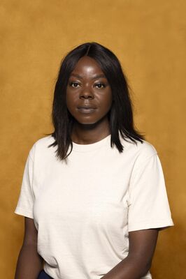 Portretfoto ensemblelid Julia Ghysels van Het Zuidelijk Toneel, die poseert tegen een okergele achtergrond.