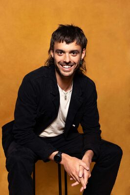 Portretfoto maker Koen van Seuren van Het Zuidelijk Toneel, voorover gebogen poserend tegen een okergele achtergrond.