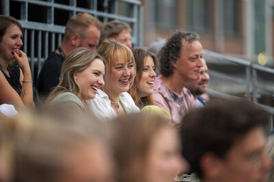 Een groep toeschouwers zit op tribunes buiten en reageert lachend op de voorstelling tijdens Theaterfestival Boulevard.