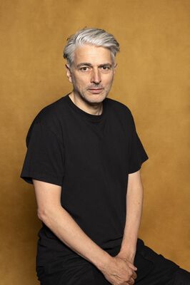 Portretfoto maker Peter Seynaeve van Het Zuidelijk Toneel, poserend tegen een okergele achtergrond.