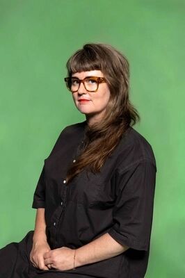 Portretfoto maker Sarah Moeremans van Het Zuidelijk Toneel, poserend tegen een groene achtergrond.