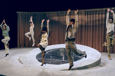 Vijf dansers in stijlvolle kostuums voeren een energieke choreografie op een podium uit.