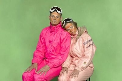 Twee personen met fel roze ski pakken en ski brillen voor een groen doek.
