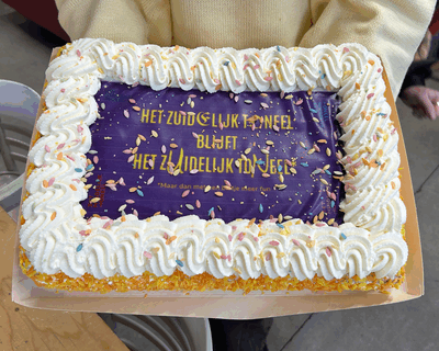 Persoon houdt slagroomtaart vast met confetti erop. Op de taart staat geschreven 'Het Zuidelijk Toneel blijf Het Zuidelijk Toneel'.