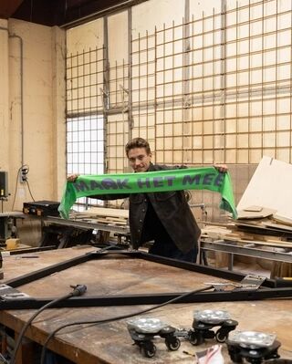 Man poseert in technische ruimte met groen-paarse supporterssjaal van Het Zuidelijk Toneel, die hij schuin omhoog houdt.